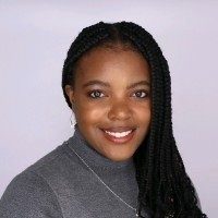 Young black woman with long, dark braids, smiling, wearing a grey turtleneck against a light background